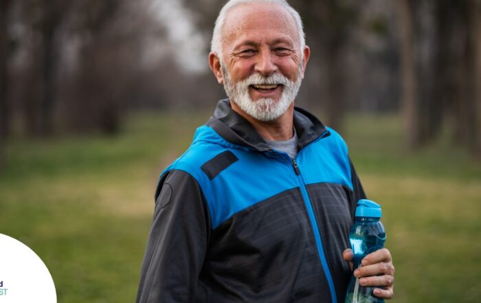 An older man smiles with a water bottle while exercising, representing the benefits of encouraging exercise when caring for seniors at home.