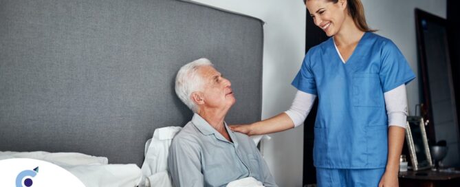 A caregiver smiles at an older client in bed, representing the compassion involved in being a live-in caregiver.