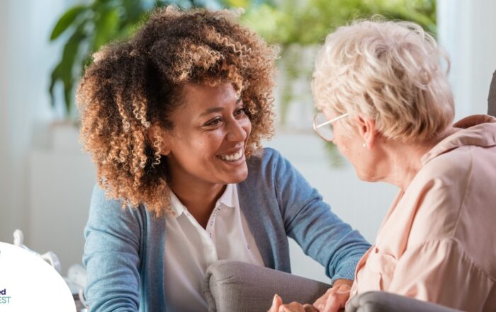 A caregiver smiles at an older client in a chair, representing the joy that can come from a healthy work-life balance.