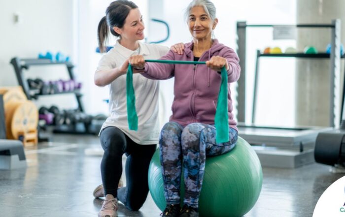 A care provider helps an older woman exercise with a resistance band and an exercise ball, representing how exercise can help with senior fall prevention.